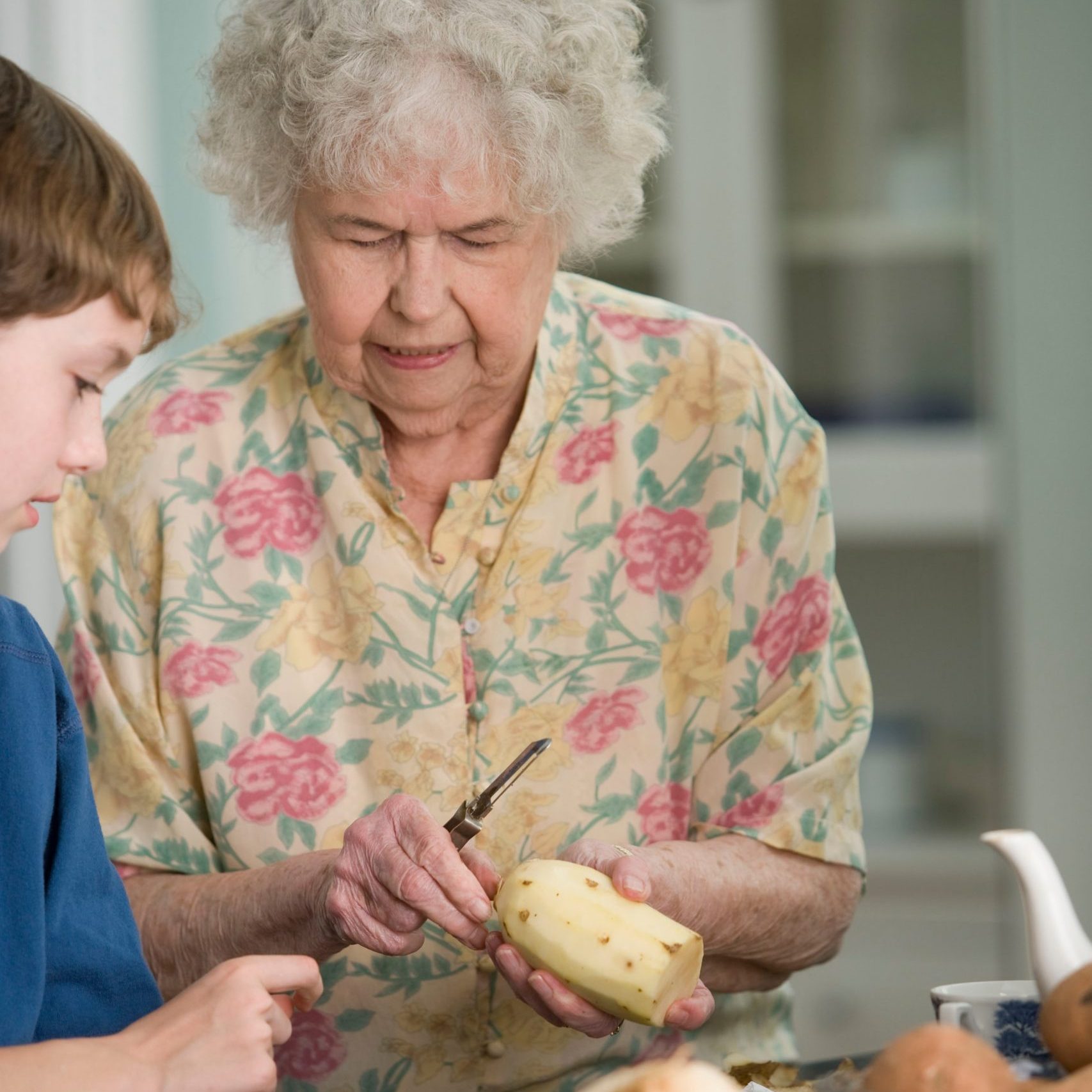 Old woman peeling potatoes with a young boy.